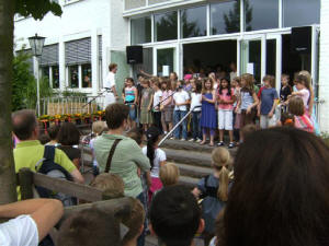 Optreden van het schoolkoor onder leiding van de Heer Jaspers, de schulleiter himself, de Hr Jaspers staat bovenaan de trappen links met het witte hemd.